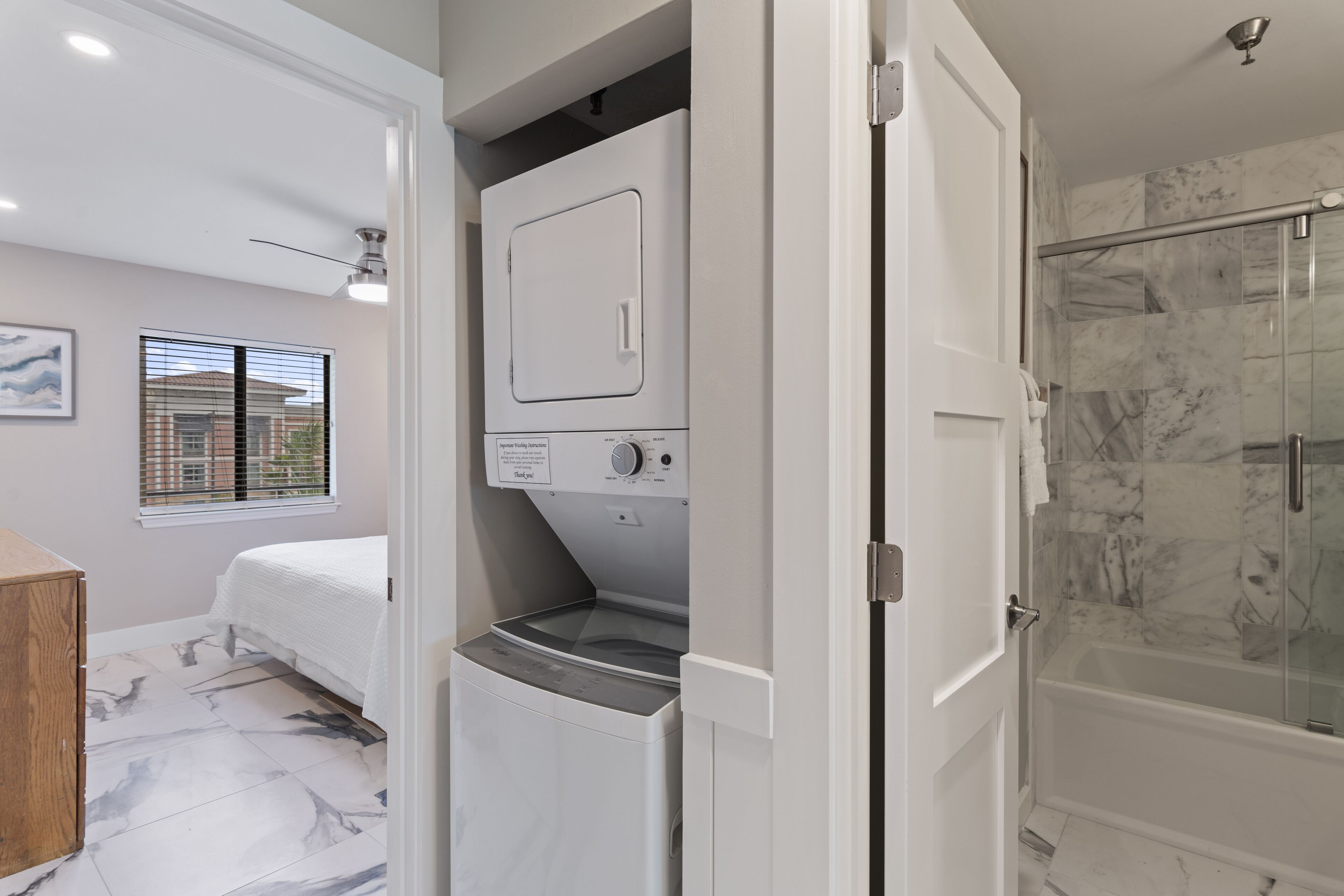 A modern bathroom with a glass-enclosed shower, a built-in washing machine, and a bed with a view of the outside.