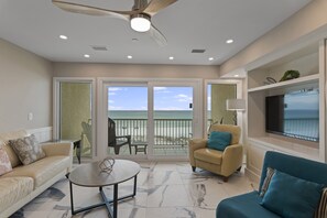A spacious living room with a large window overlooking a balcony, a ceiling fan, and a flat-screen TV mounted on the wall.