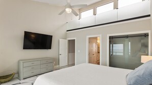 Een slaapkamer met een bed, een televisie, een plafondventilator, een kledingkast en een badkamer die door een open deur zichtbaar is.
