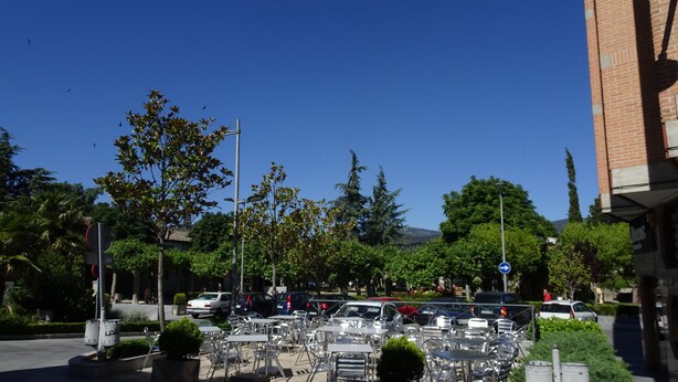 An outdoor seating area with tables and chairs, surrounded by trees and parked cars. - Hostal Gonzalez (Guadarrama)