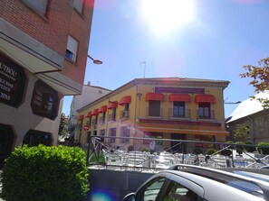 A yellow building with red awnings, a sign for a bar, cafeteria, and restaurant, and a parked car in front. - Hostal Gonzalez (Guadarrama)