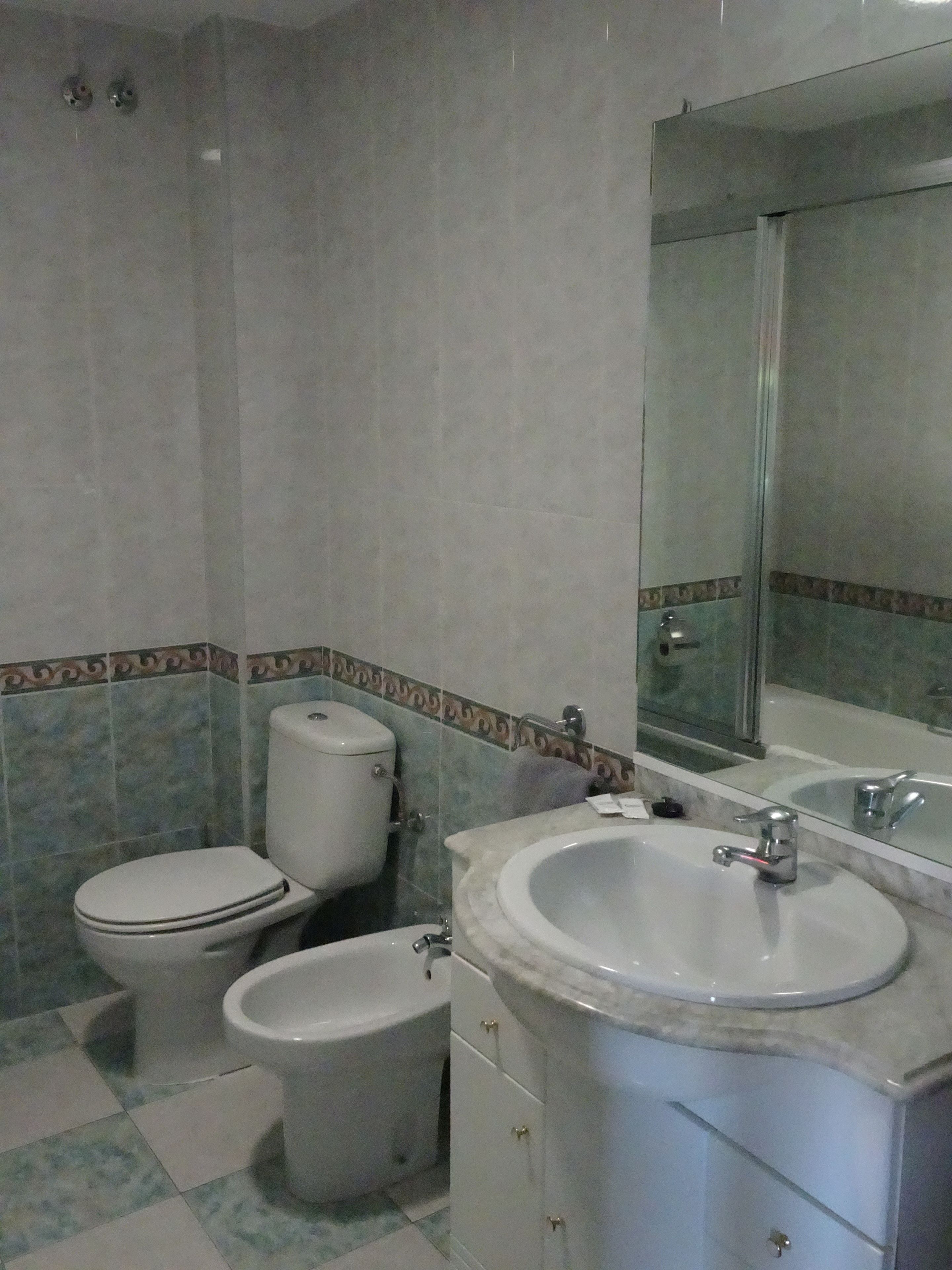A bathroom with a toilet, bidet, sink, and mirror.