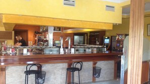 A bar area with a counter, stools, and a person working behind it. - Hostal Gonzalez (Guadarrama)