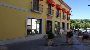 A yellow building with red awnings, a sign reading "Charmeria," and outdoor seating with tables and chairs. - Hostal Gonzalez (Guadarrama)