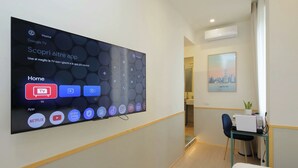 A hotel room with a large TV displaying a home screen with app icons, a desk with a laptop, and a chair. - Proja Housing Romagnosi 20 (Rome)