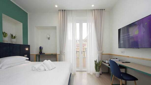 A modern hotel room with a bed, a desk, a chair, a TV, and a balcony view. - Proja Housing Romagnosi 20 (Rome)
