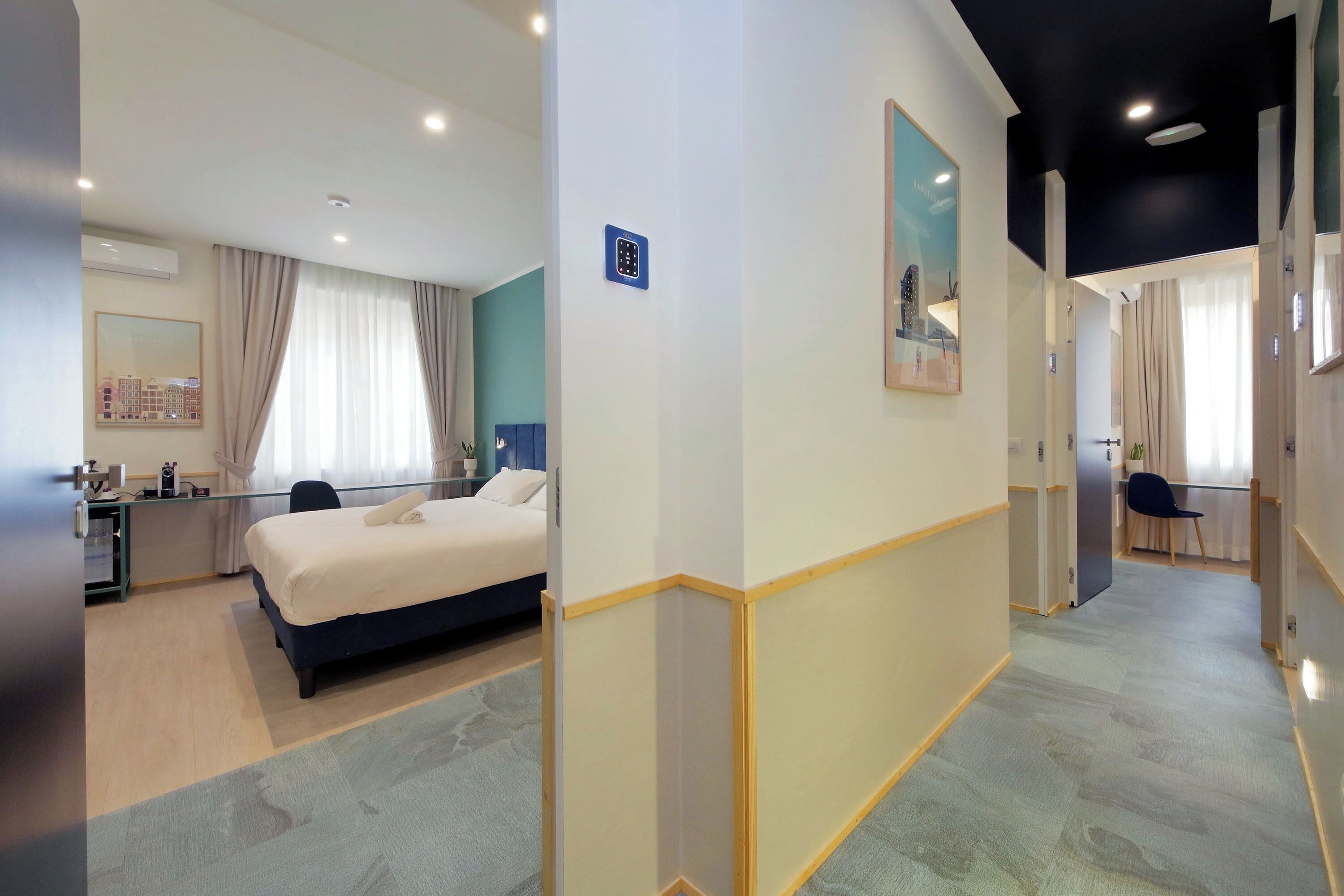 A hotel room with a bed, desk, and chair, a mirror, and a view of the cityscape through the window.