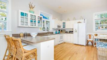 A spacious kitchen with white cabinetry, a central island, and a dining area with wicker furniture.