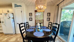 Un coin repas avec une table ronde, des chaises noires, des sets de table bleus, un lustre et une vue par la fenêtre.