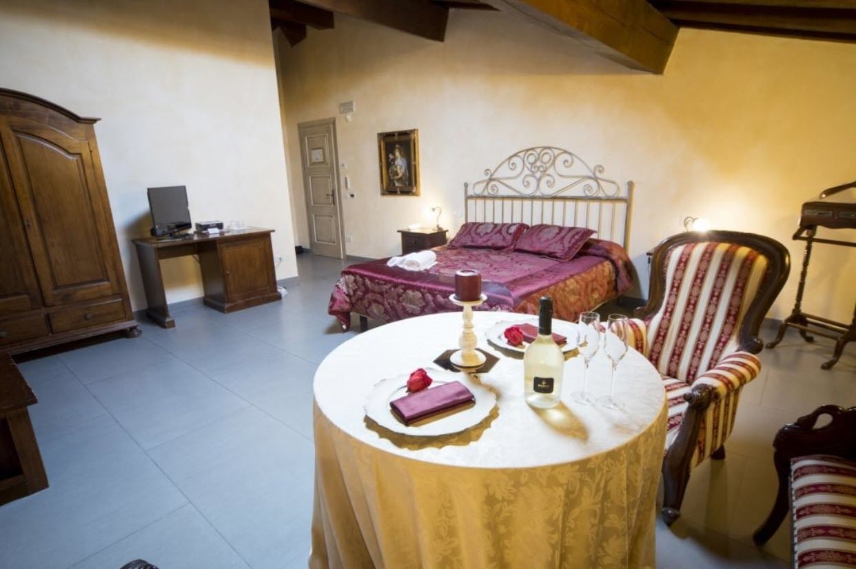 Ein Schlafzimmer mit einem Bett, einem Nachttisch, einem Sessel und einem runden Tisch mit einer Flasche und Gläsern.