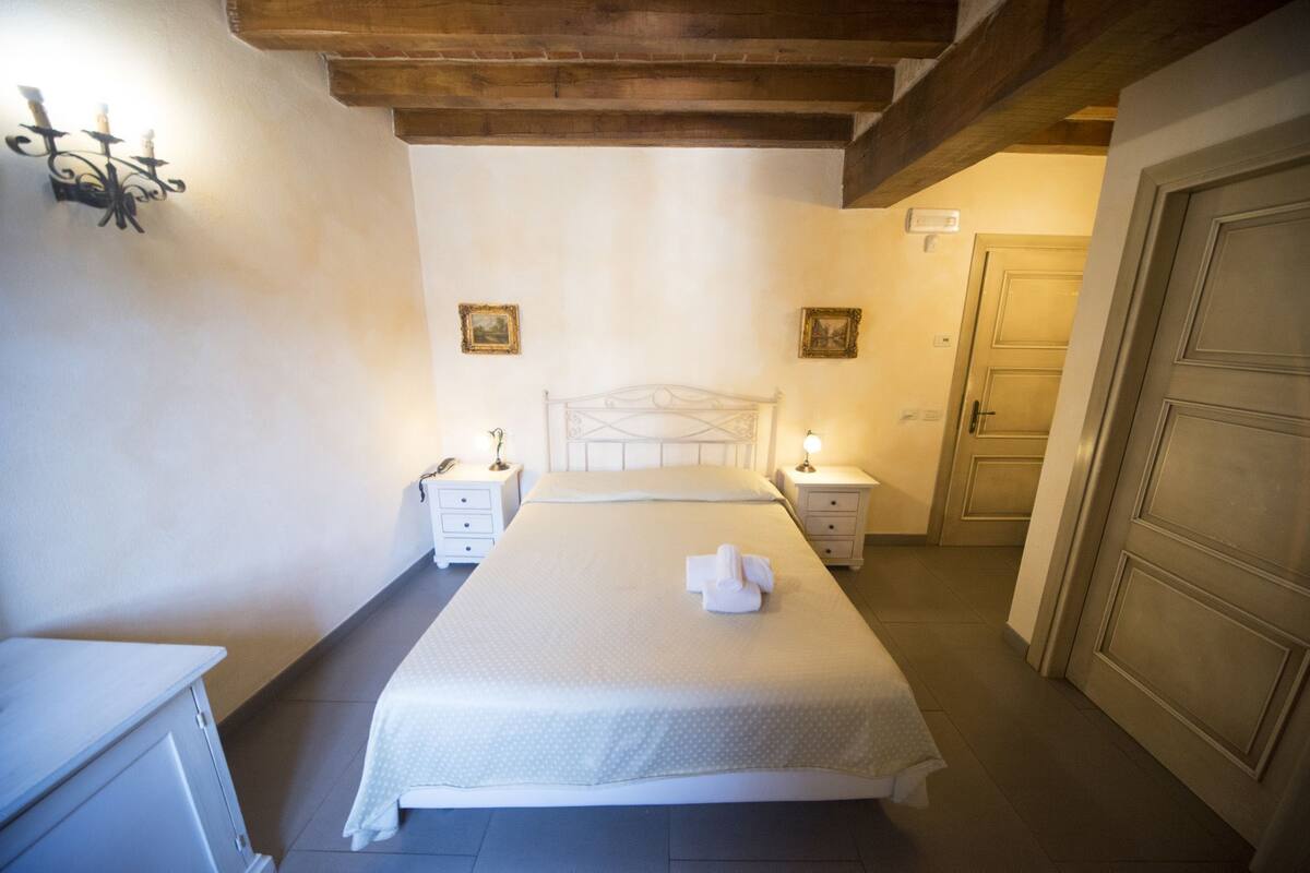 Ein Schlafzimmer mit einem Bett, Nachttischen, einer Ablage, einer Tür und einer Wandleuchte.