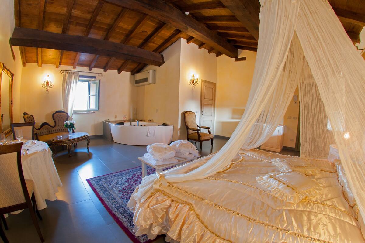 Ein Schlafzimmer mit Baldachinbett, einer Sitzecke mit Stühlen, einem Tisch und einer Badewanne.
