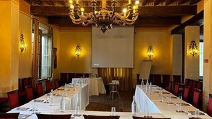 A conference room with long tables, red patterned chairs, a chandelier, and a projector screen. - La Tavola Rotonda (Cortemaggiore)
