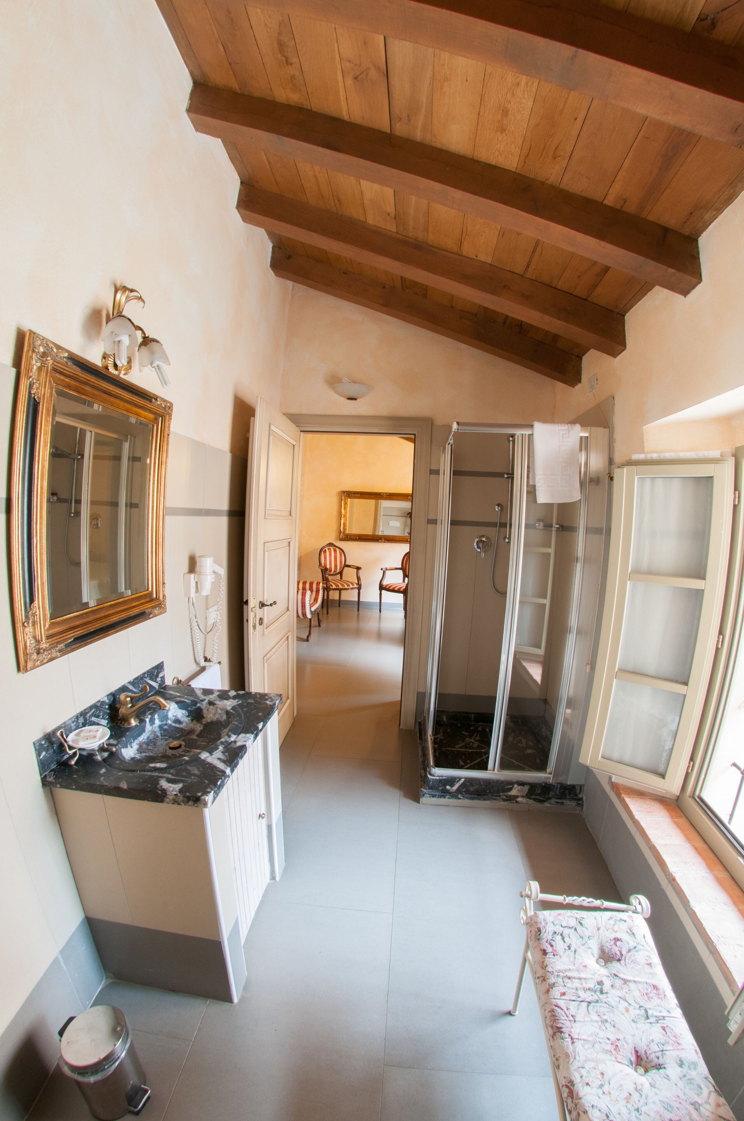 Une salle de bain avec un comptoir en marbre, un grand miroir, une cabine de douche et un banc près de la fenêtre.