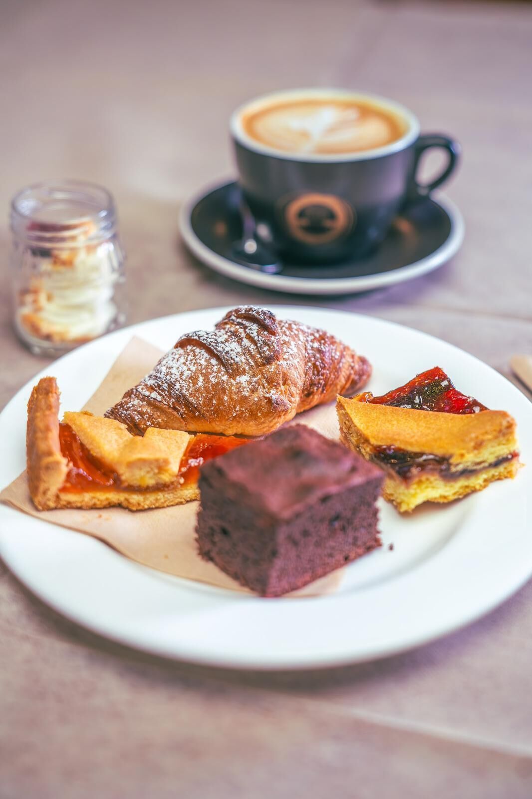 A plate with a croissant, a slice of pie, and a piece of cake, along with a cup of coffee on a saucer.