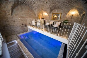 A swimming pool with a tiled edge and a white railing, surrounded by stone walls and a wooden staircase. - La Tavola Rotonda (Cortemaggiore)