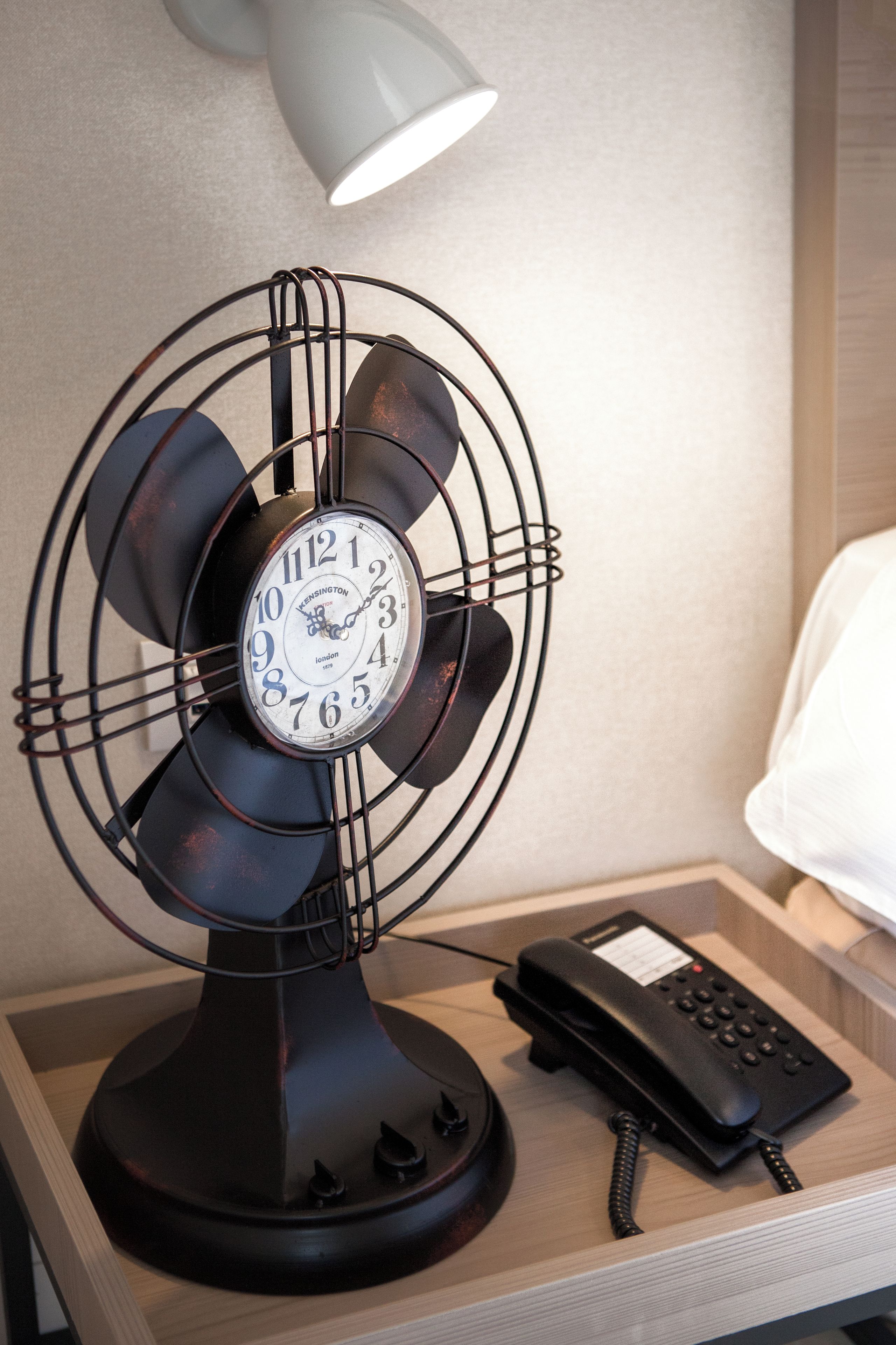A vintage-style fan with a clock on a bedside table, next to a telephone.
