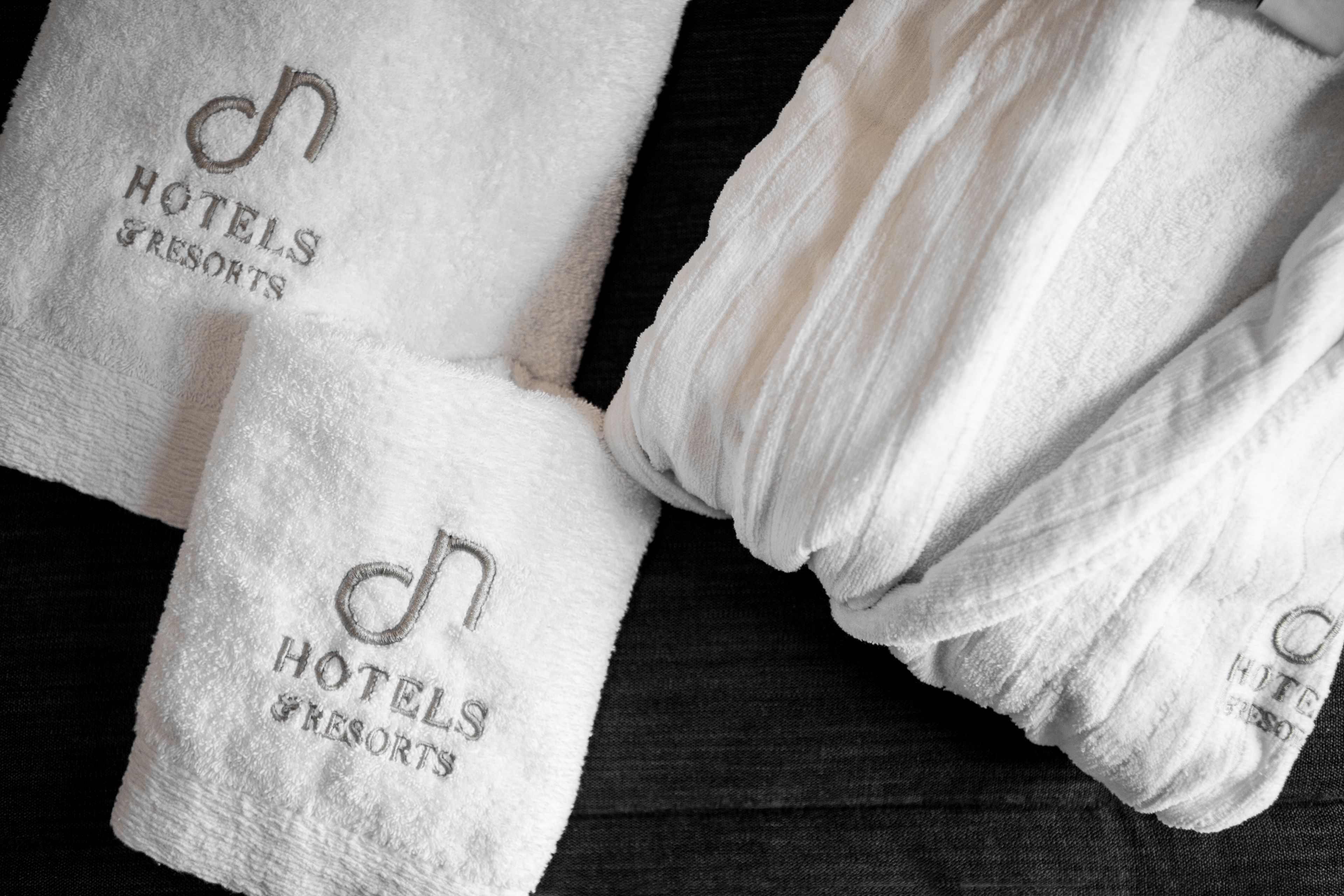 Tre pænt foldede hvide håndklæder med præget tekst, der angiver, at de stammer fra et hotel eller resort.