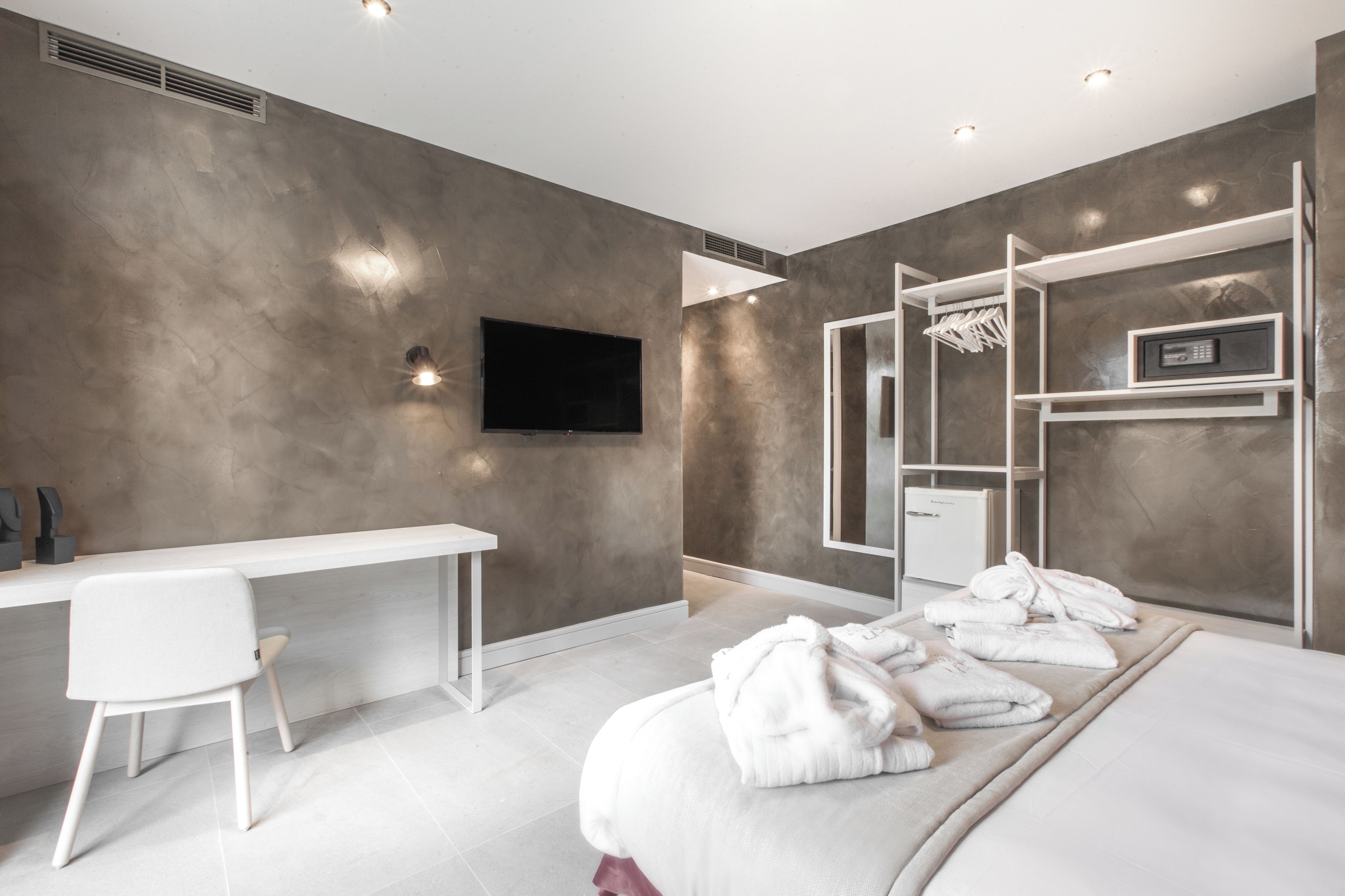 A modern hotel room with a bed, a desk, a TV, and a wardrobe.