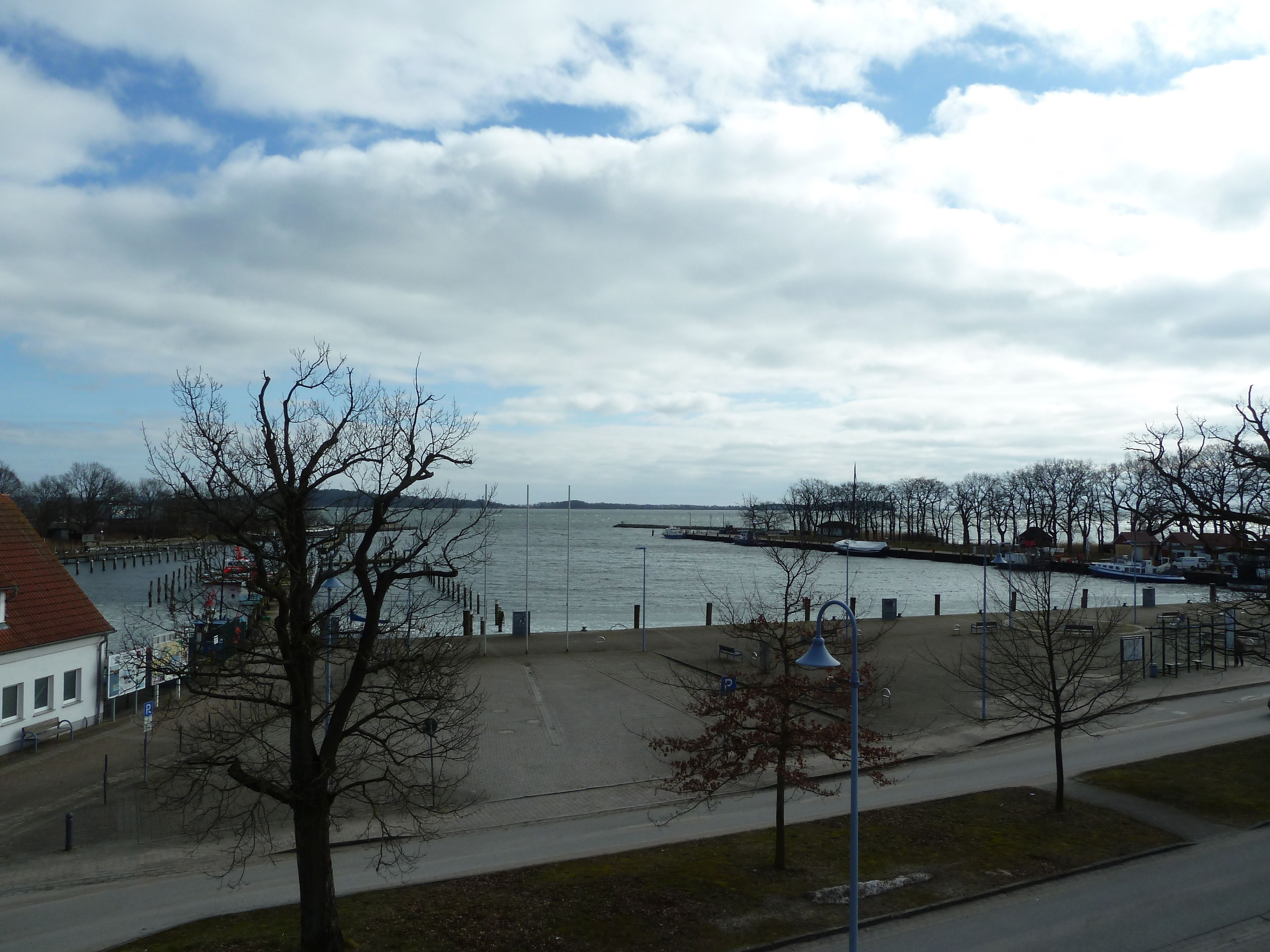 A waterfront view with a dock, a pedestrian path, and a row of buildings.