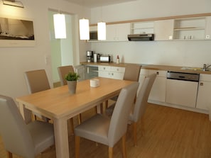 A modern kitchen with a wooden table and chairs, a coffee machine, and a dishwasher. - Apartmenthaus Goor (Putbus)
