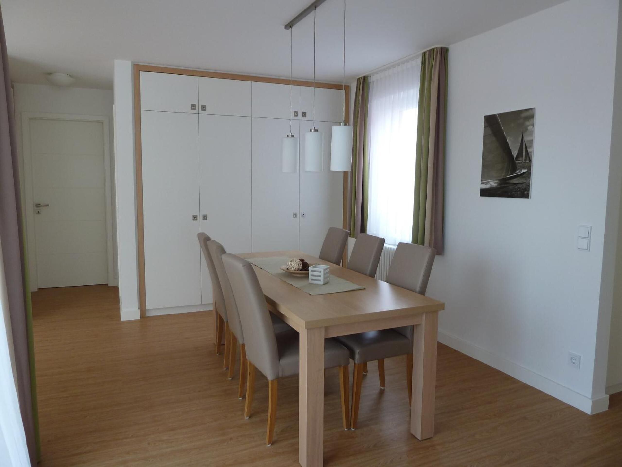 A modern dining area with a wooden table, six chairs, and pendant lights.