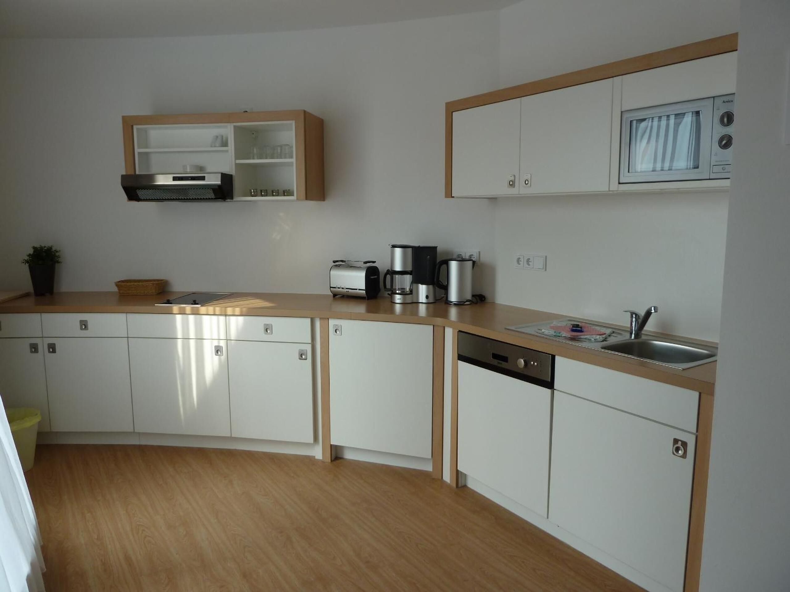 Cocina moderna con armarios blancos, encimera de madera, microondas integrado y cafetera.
