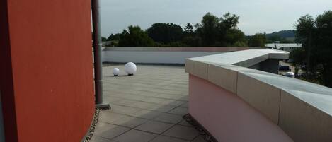 A rooftop terrace with two spherical white objects, a red wall, and a view of trees and buildings in the background.