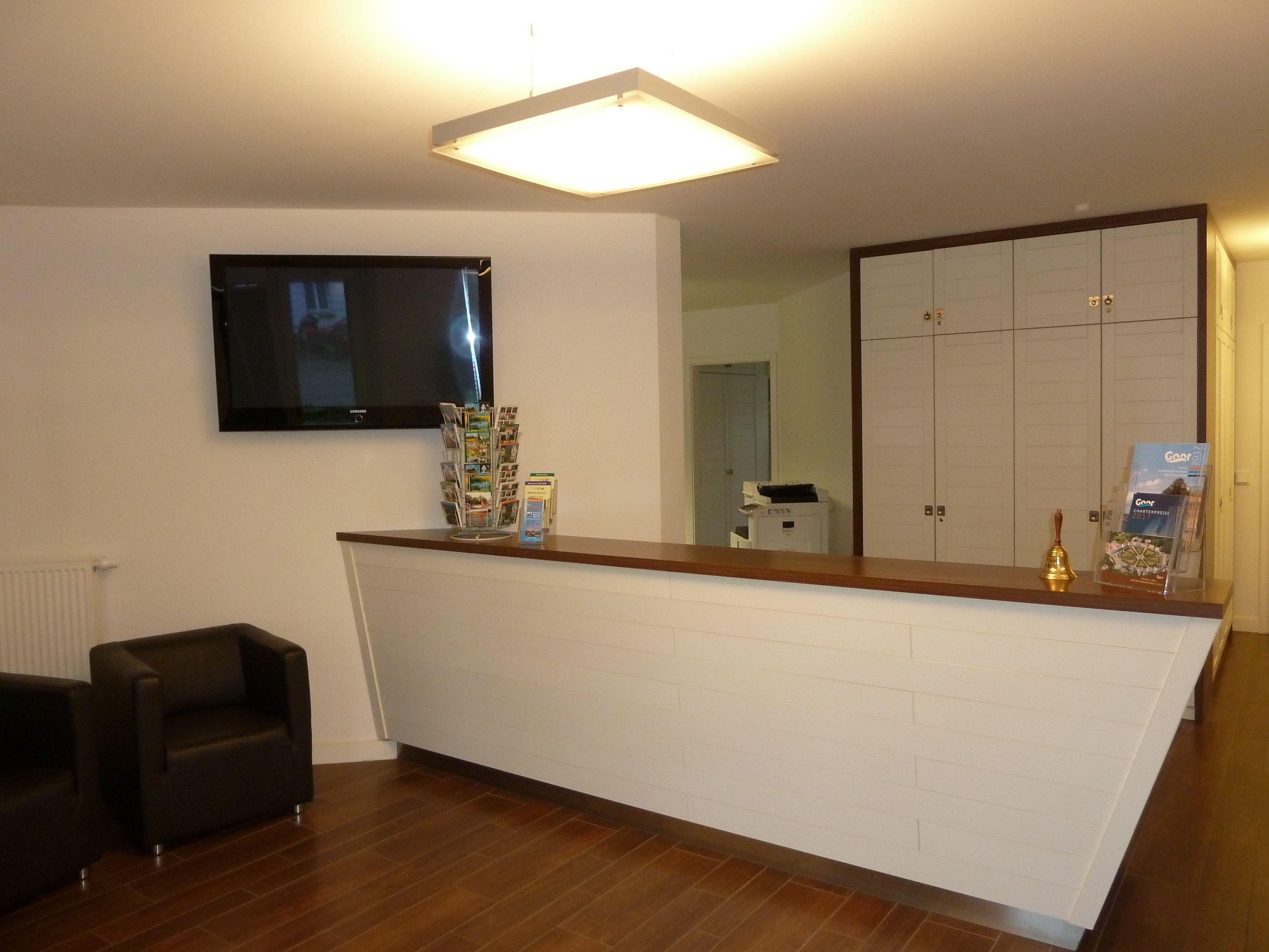 A reception area with a flat-screen TV mounted on the wall, a magazine rack, and a bell on the counter.