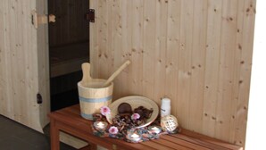 Uma sauna de madeira com banco, um balde de madeira e um aquecedor.