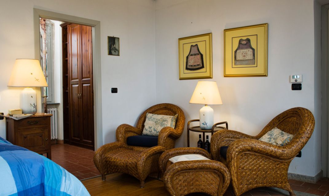 A room with two wicker chairs, a bed, a wooden wardrobe, and two wall-mounted lamps.