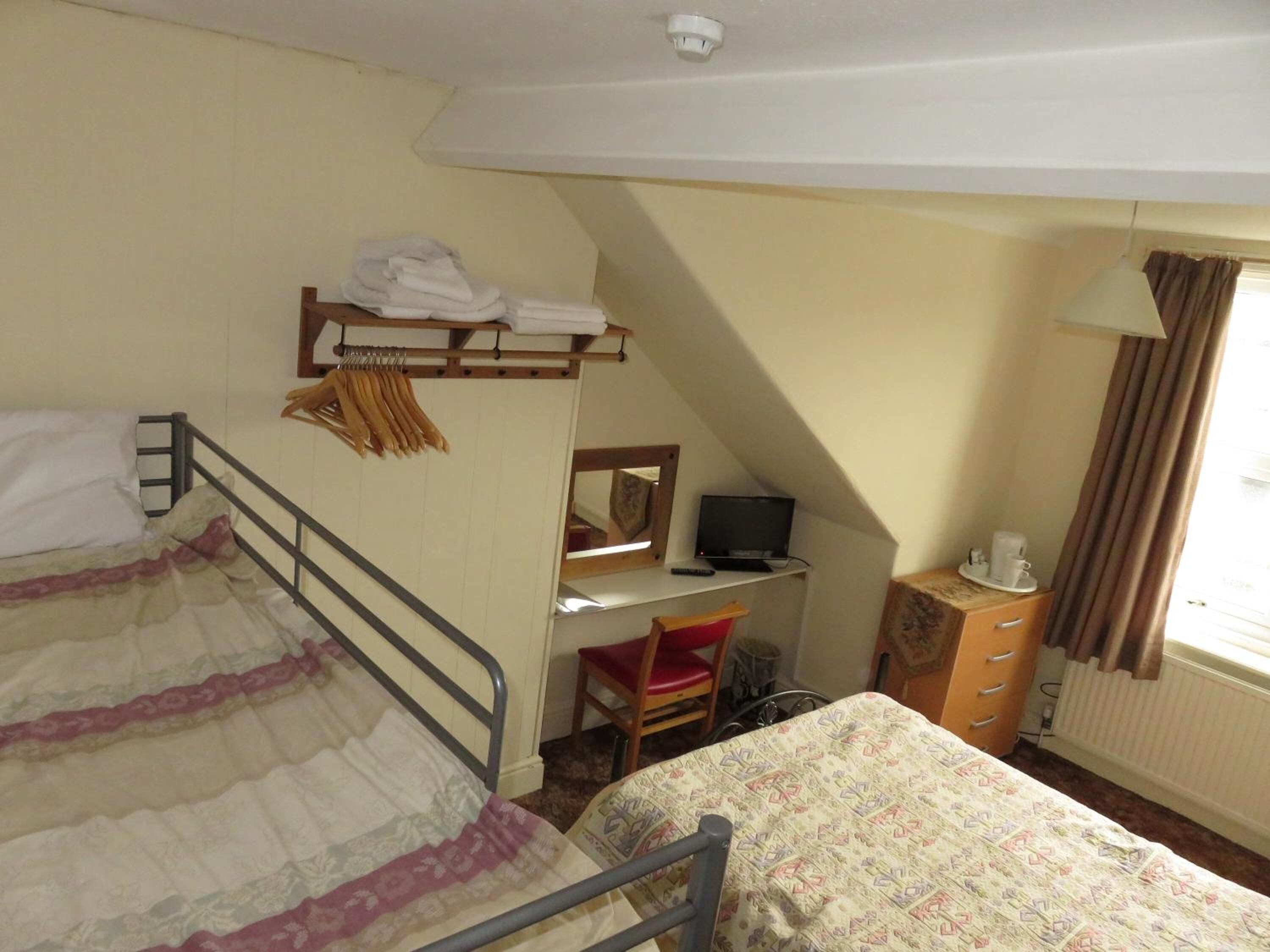 Una habitación de hotel pequeña y funcional con literas, un escritorio con computadora, una silla, una cómoda y una ventana con cortinas.