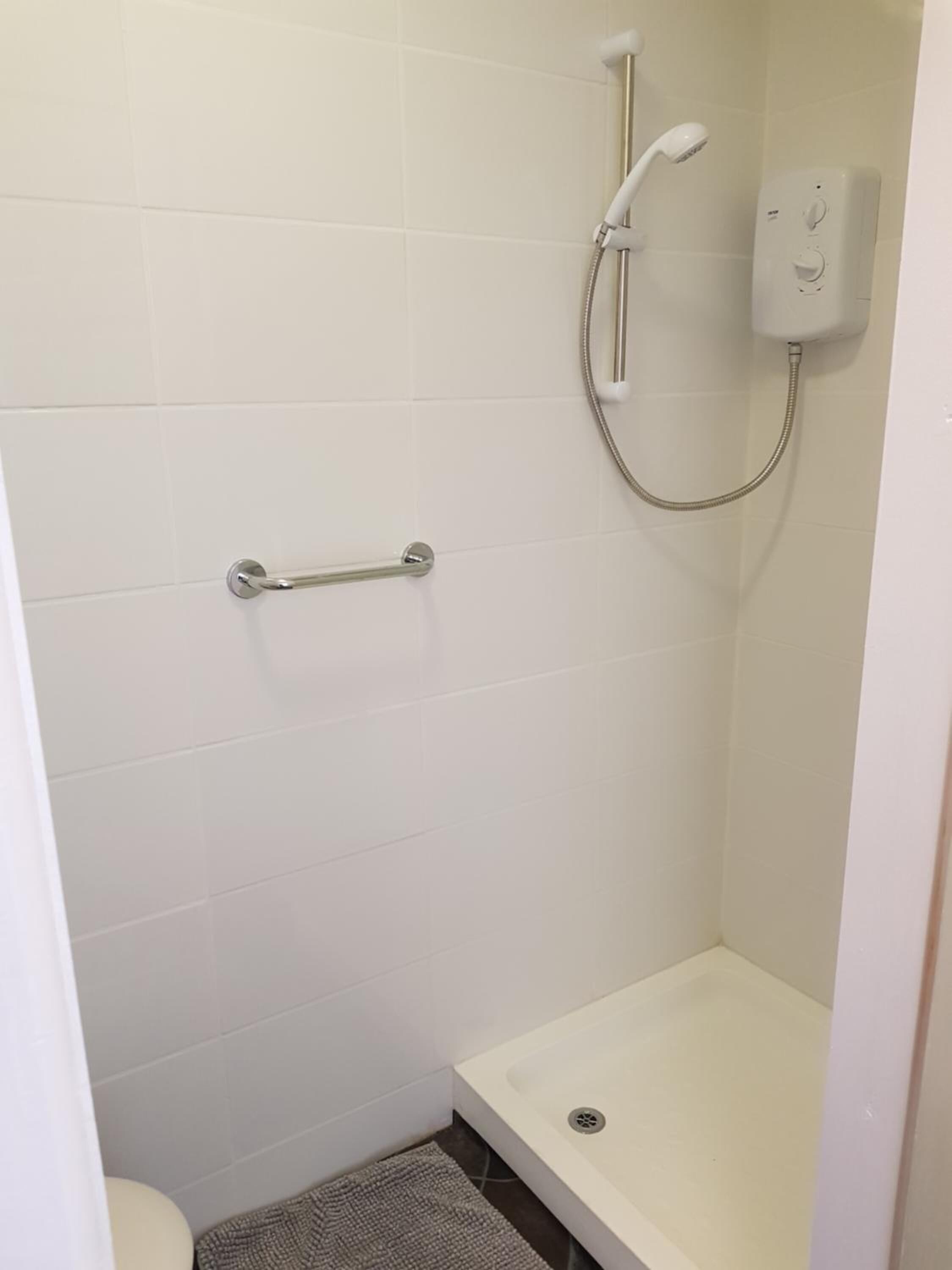 Un box de ducha pequeño con azulejos blancos, un cabezal de ducha manual y un panel de control.