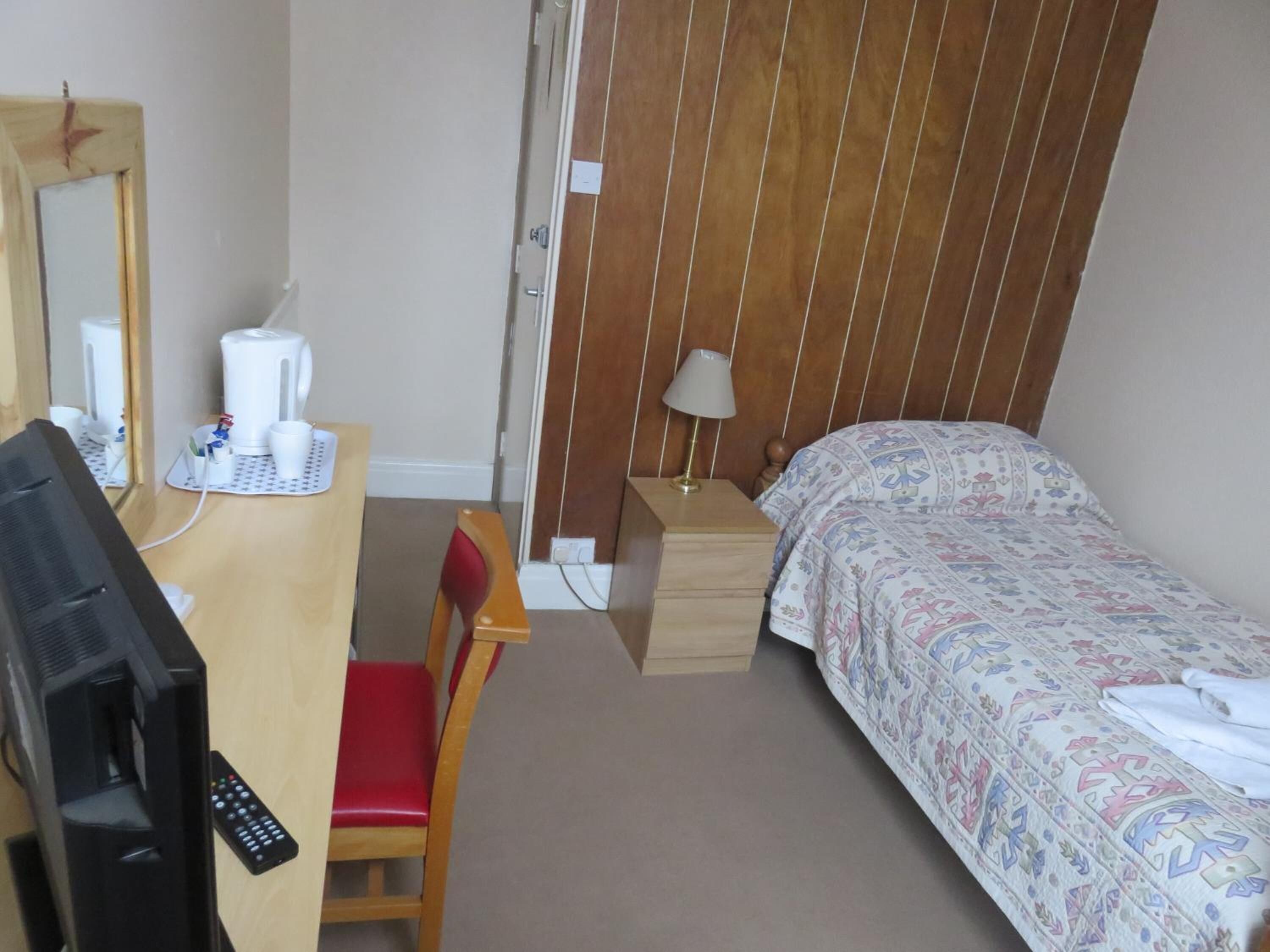 A hotel room with a desk, chair, bed, and a TV.