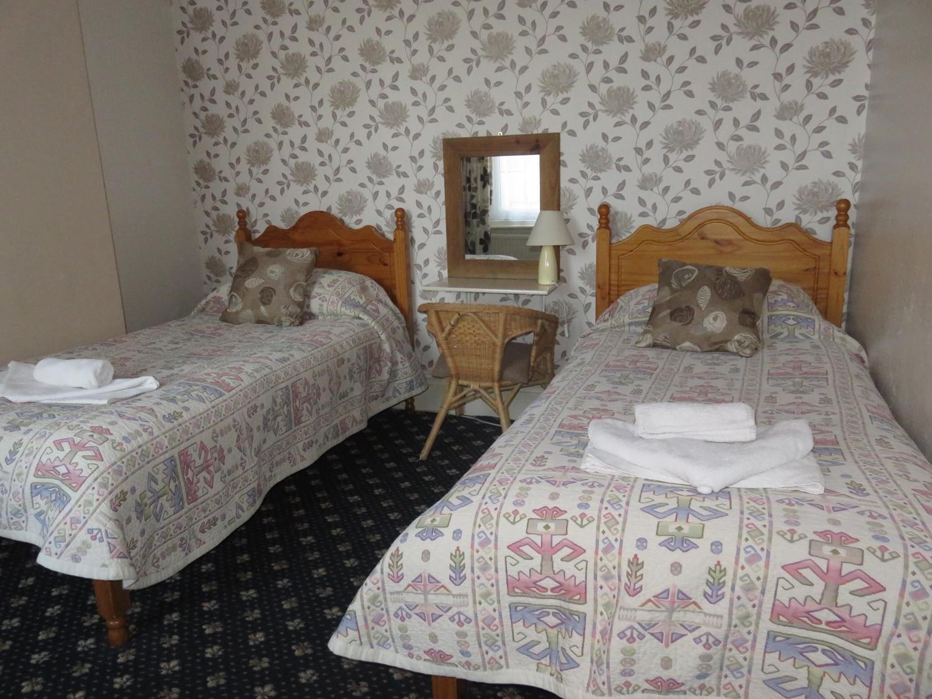 Una habitación con dos camas individuales, una mesita, una silla y un espejo en la pared.