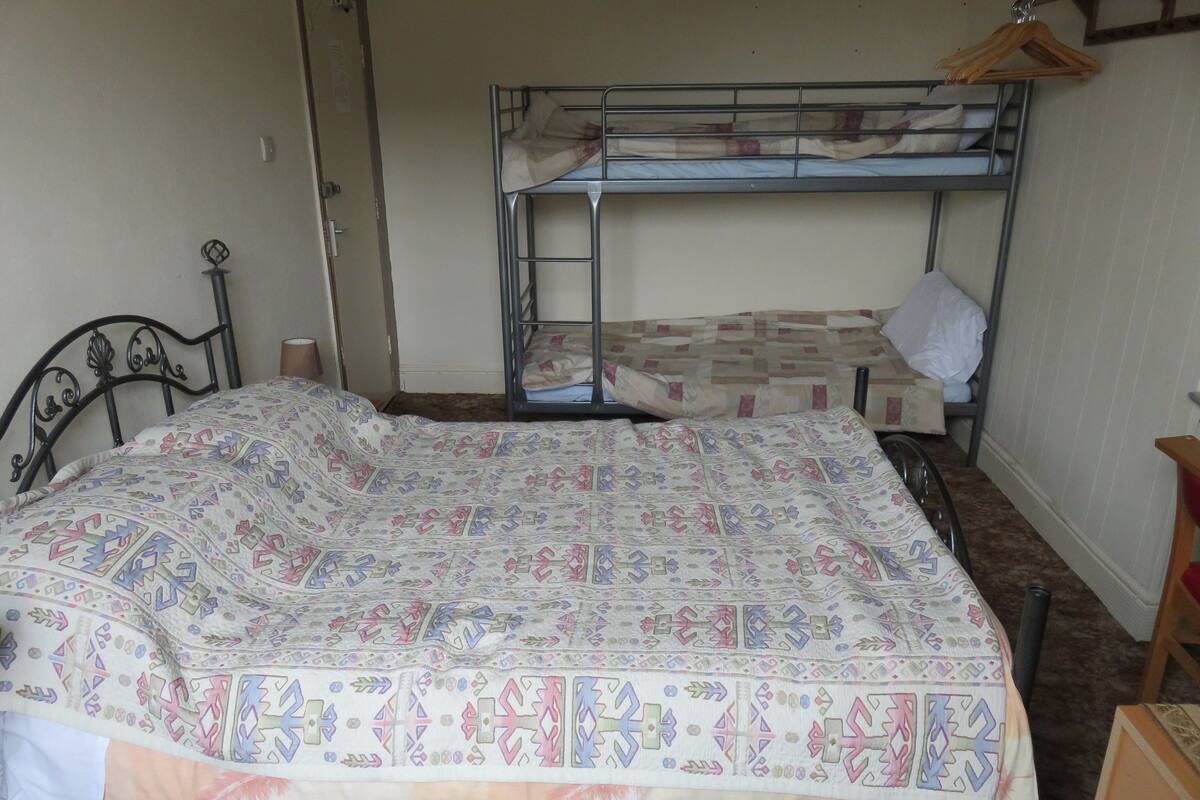 A single bed with a patterned bedspread and a bunk bed in the background.