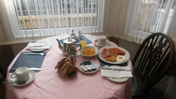 A breakfast table with a pink tablecloth, plates of food, a teapot, cups, and a chair. - Glencoe Hotel (Bridlington)