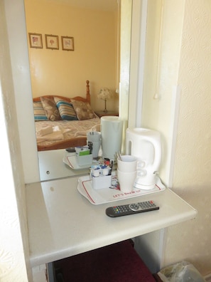 Ein Hotelzimmer mit einem Bett, einem Nachttisch mit Fernbedienung, einer Kaffeemaschine und einem Tablett mit Tassen und einer Kanne.