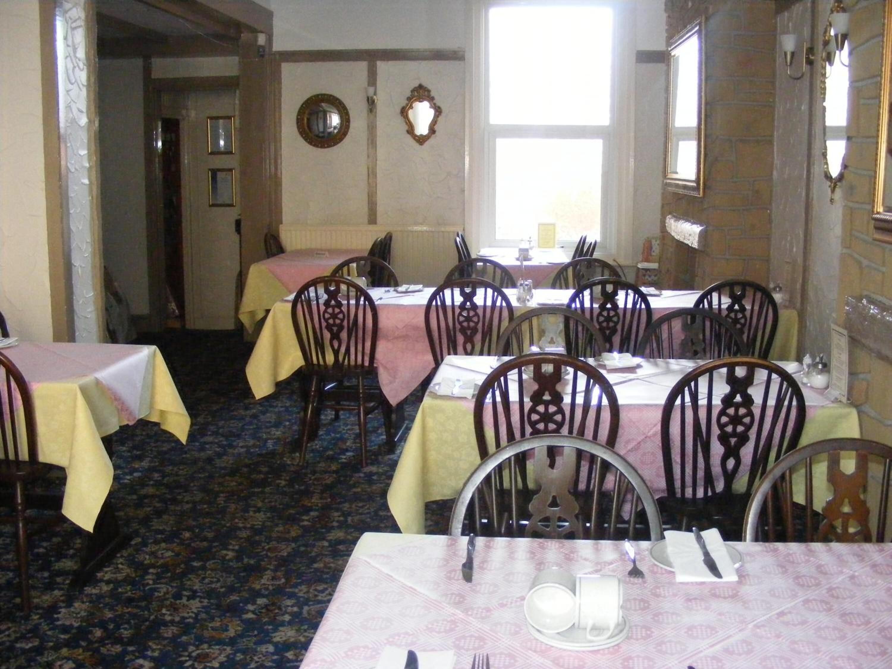 A dining area with multiple tables and chairs, a patterned carpet, and a window with natural light.