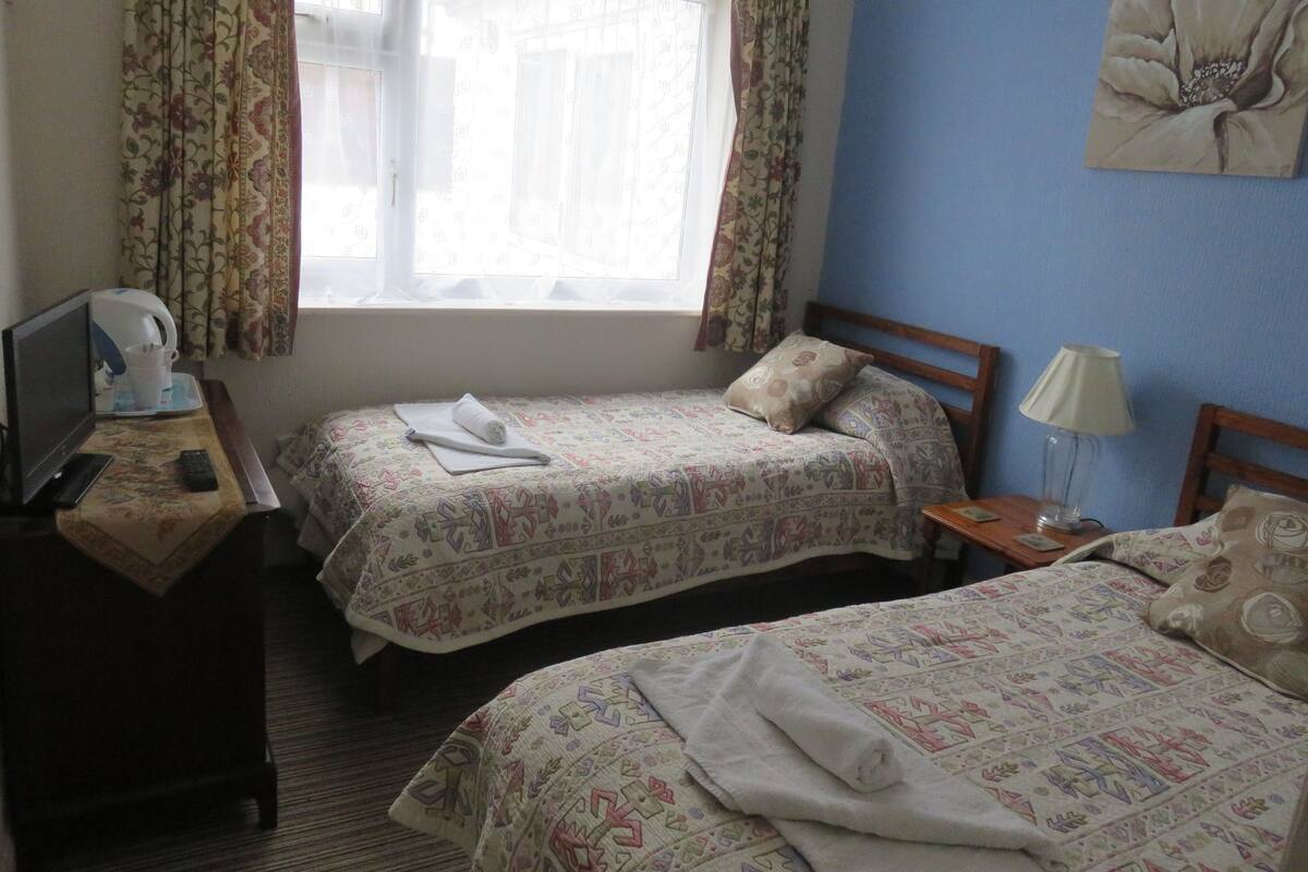 A hotel room with two beds, a TV, a lamp, and a window with curtains.