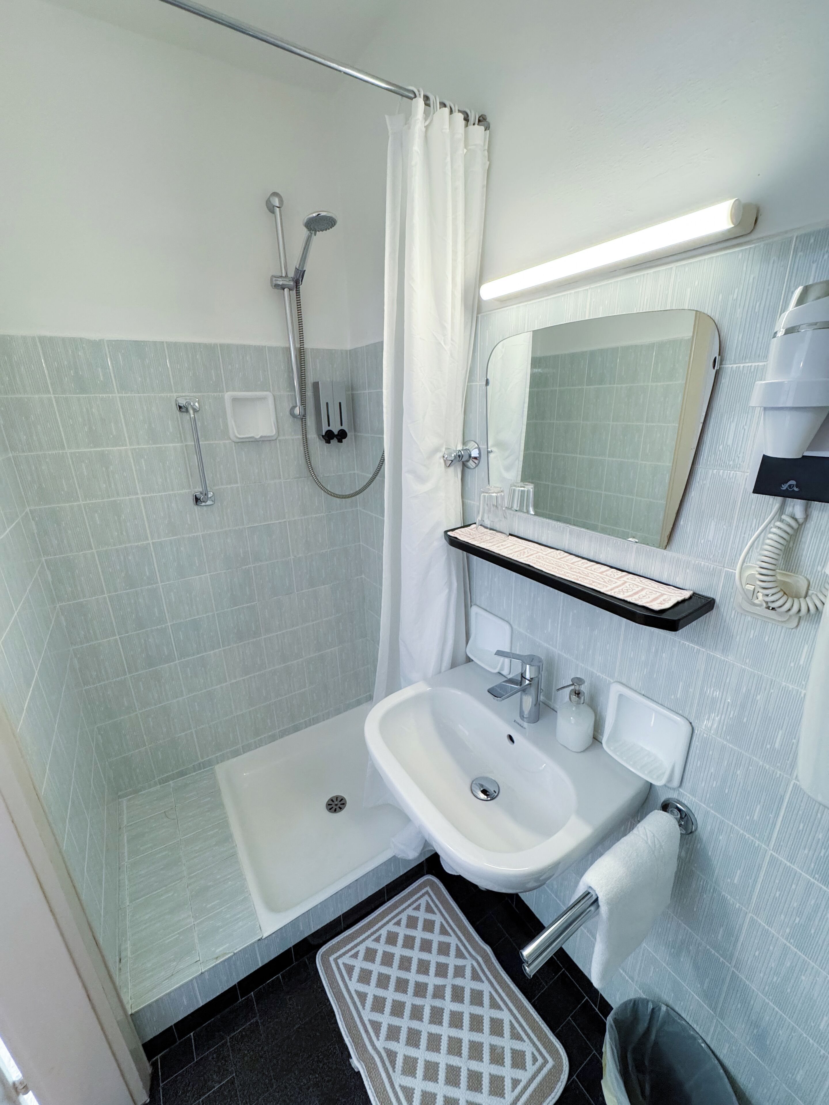 A modern bathroom with a shower, a sink, a toilet, and a mirror.