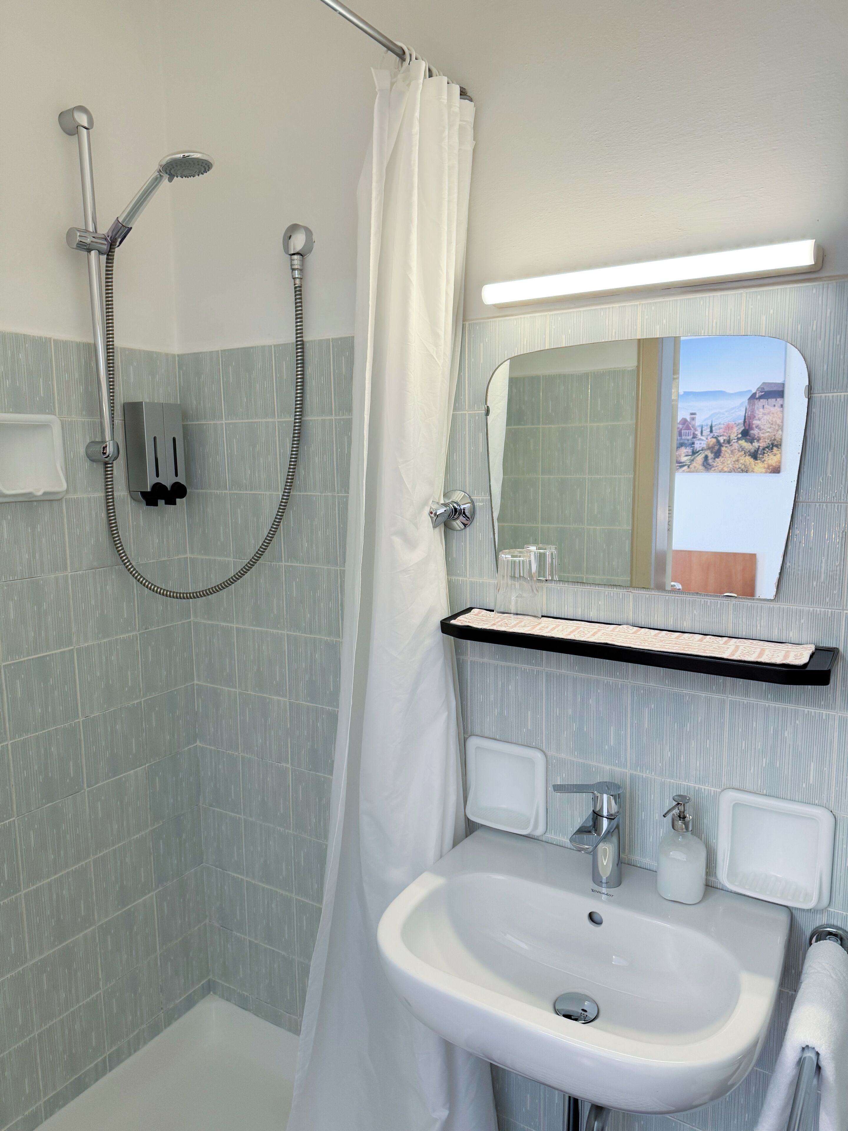 Ein Badezimmer mit Dusche, Waschbecken, Spiegel und Handtuchhalter.