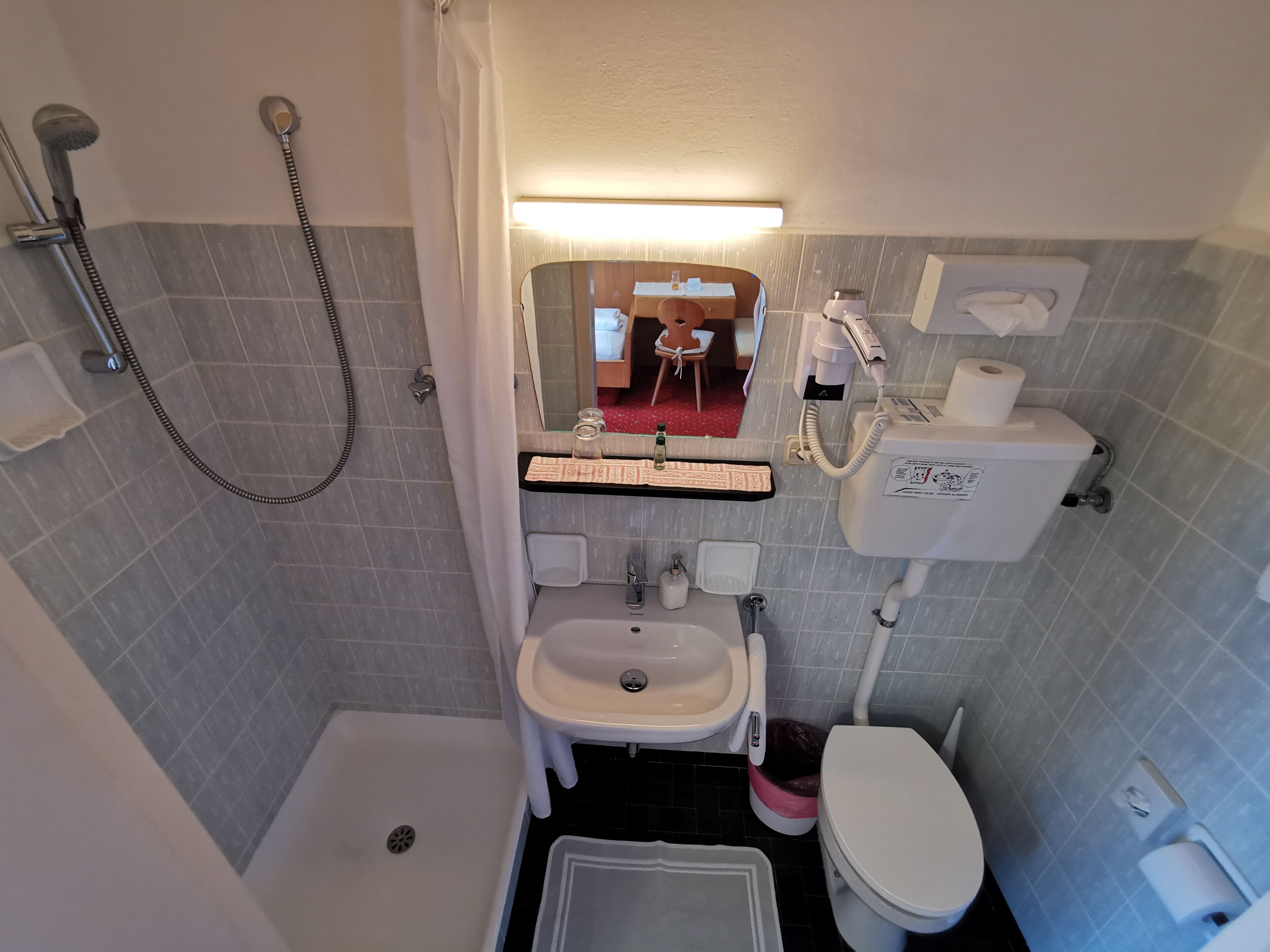 A bathroom with a shower, toilet, sink, and a mirror.