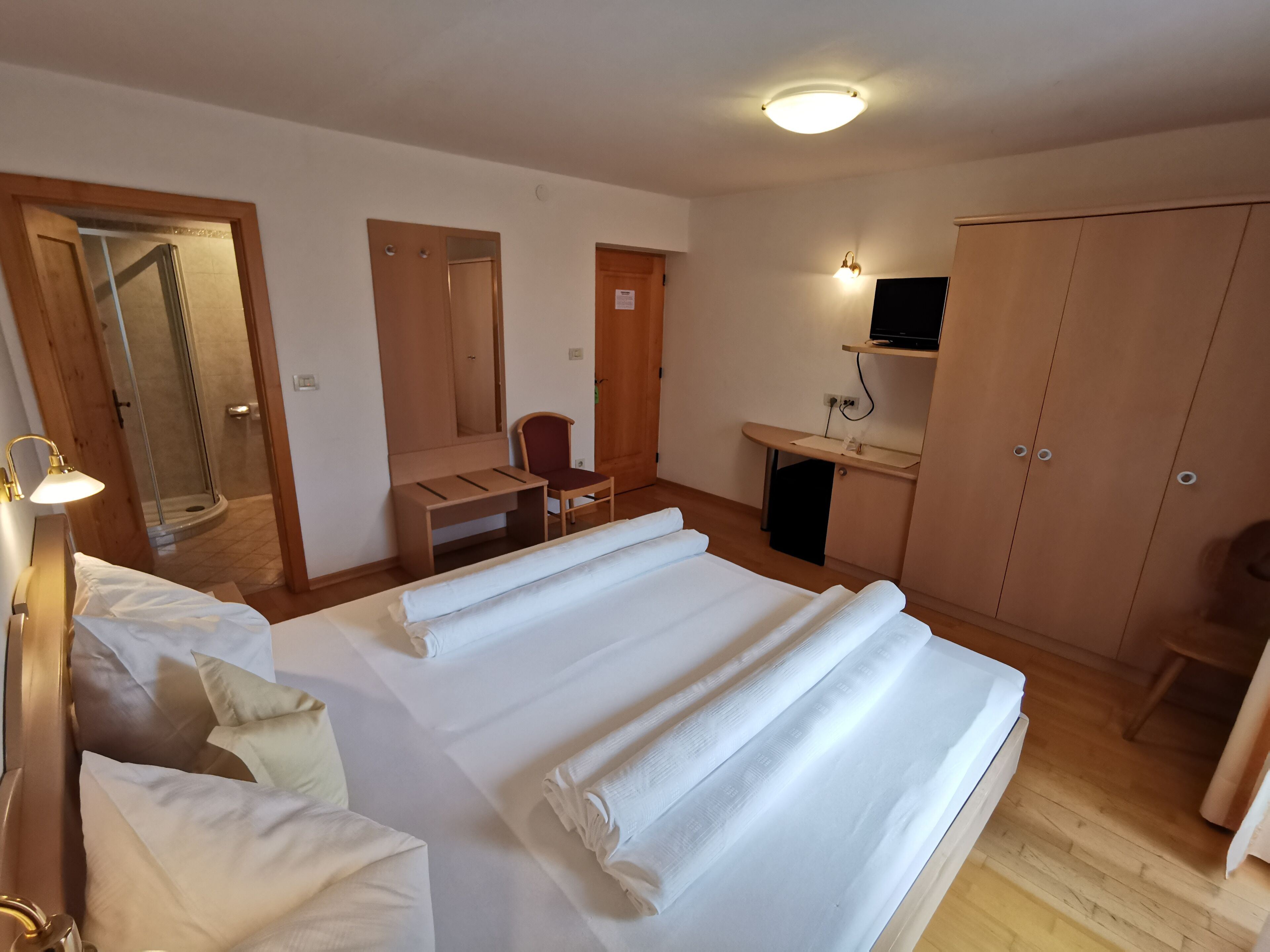 A hotel room with a bed, a desk, a chair, a wardrobe, and a shower area.