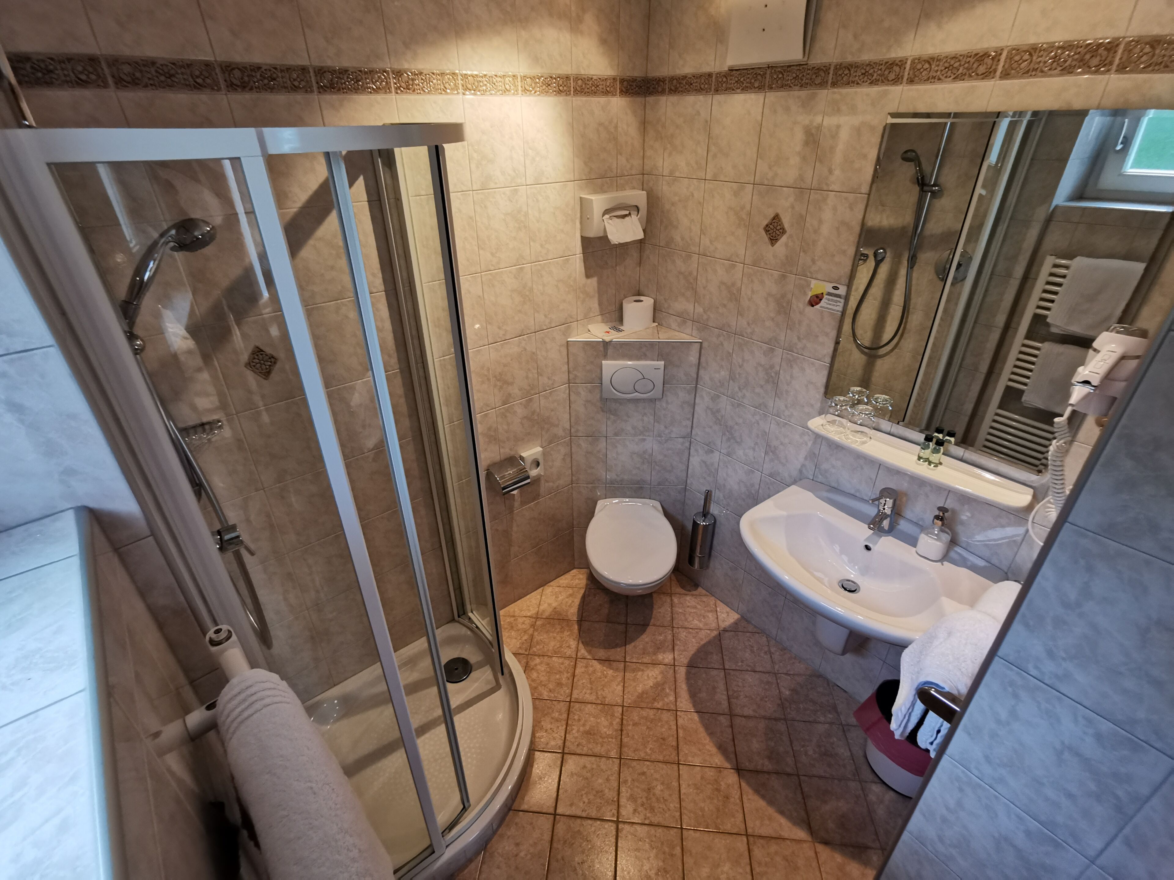 Un baño moderno con ducha envuelta en vidrio, inodoro, lavamanos y espejo.