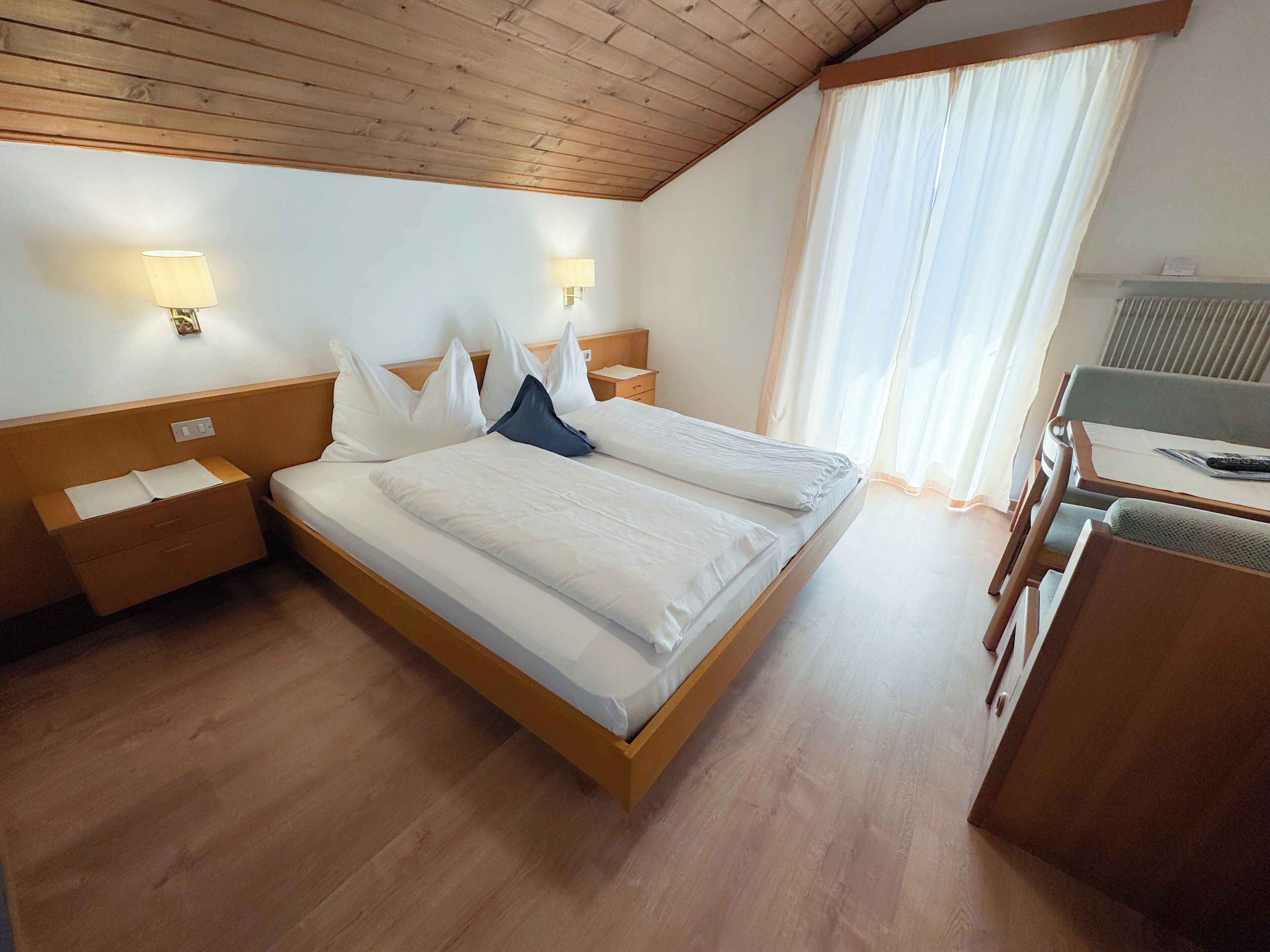 A hotel room with a wooden bed, bedside tables, a desk, and a chair.