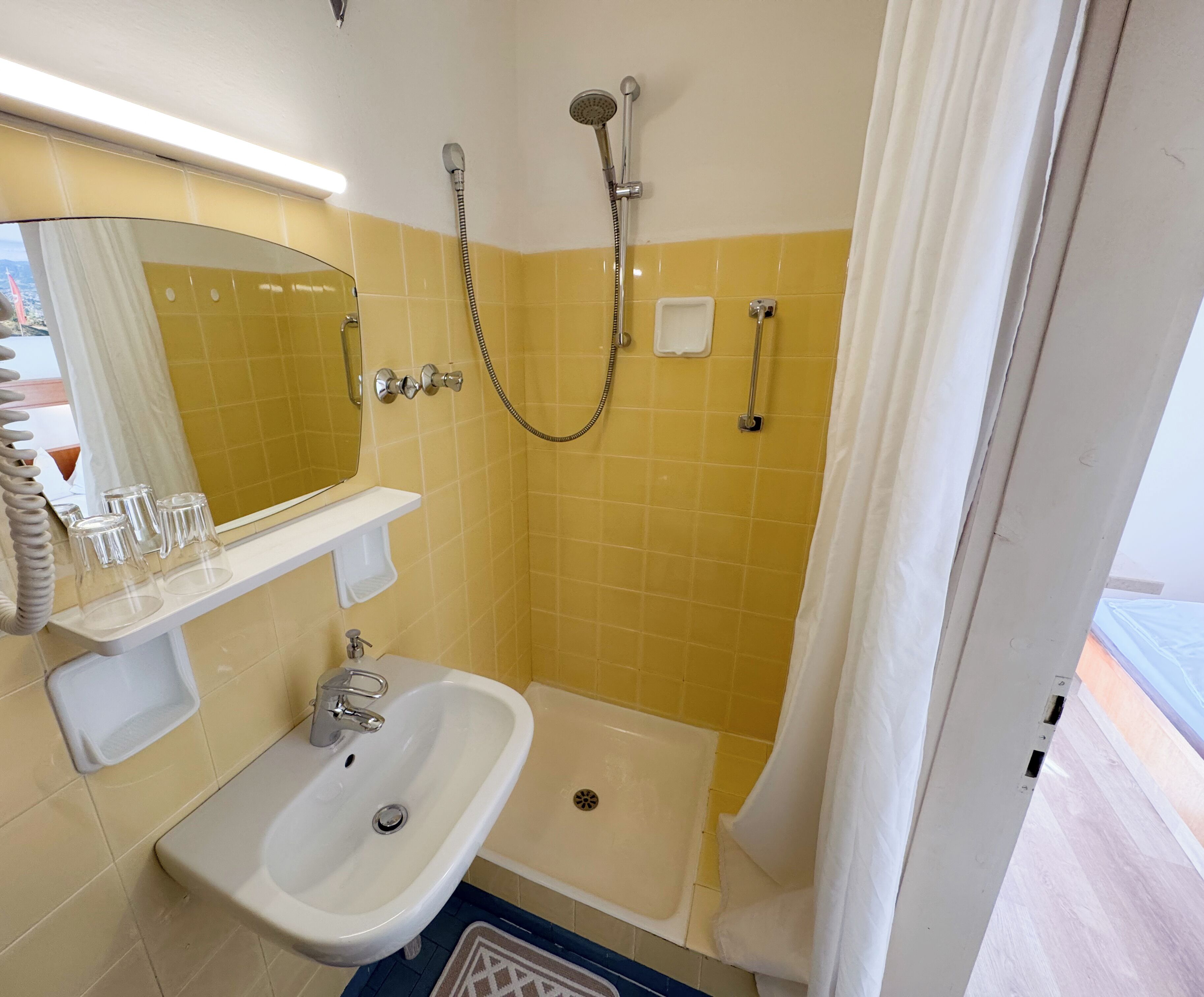 A bathroom with a sink, mirror, shower, and a towel rack.