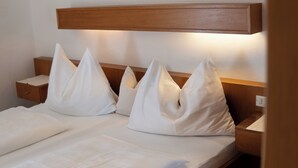 A neatly made bed with white linens and pillows, a wooden headboard, and a bedside table with a lamp. -  Active B&B Prairerhof (Schenna)