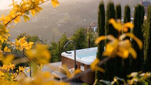 A hot tub on a deck with a view of a valley and distant buildings. -  Active B&B Prairerhof (Schenna)