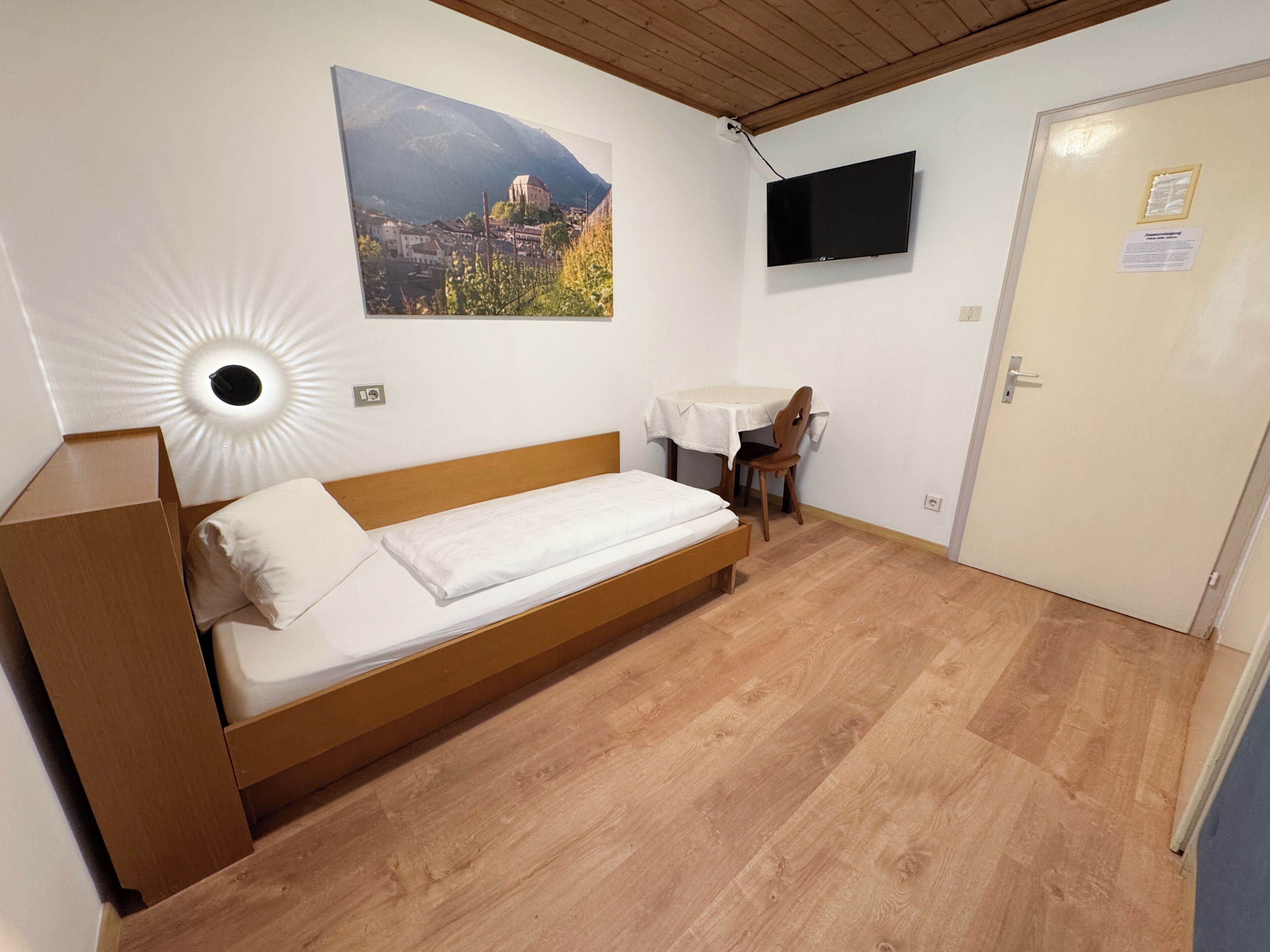 Una stanza con un letto, una scrivania, una sedia, una televisione e una porta.